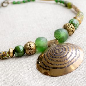 Eye catcher: Messinganhänger mit Spiralsymbol aus West-Afrika gerahmt von grünen Recyclingglas-, Keramik- und Bronzeperlen